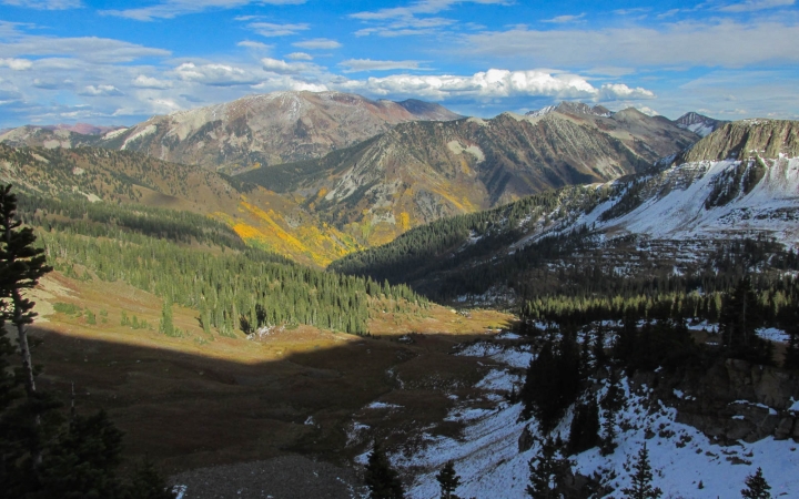 A vast mountainous landscape rests under a blue sky. There are snow in some parts of the scene. 